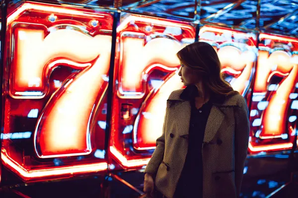 A woman smiling while playing online games on her laptop, surrounded by neon casino elements, showcasing 7D77’s diverse game collection.